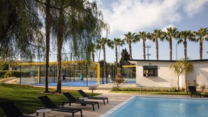 A pool area with lounge chairs, a tennis court, and palm trees. - B&B Villaseta (Agrigento)
