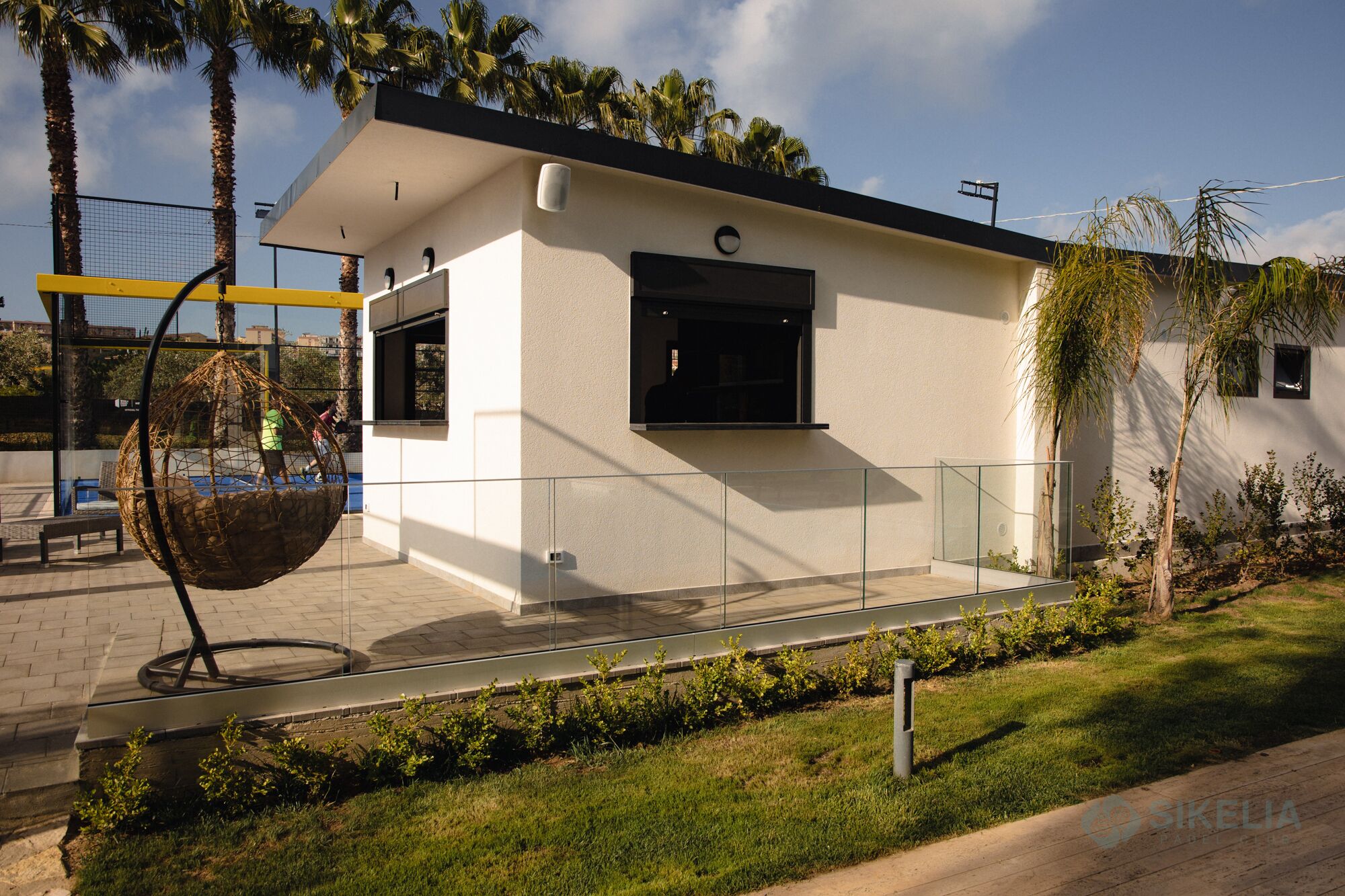 A modern building with a flat roof, large windows, and a glass railing.