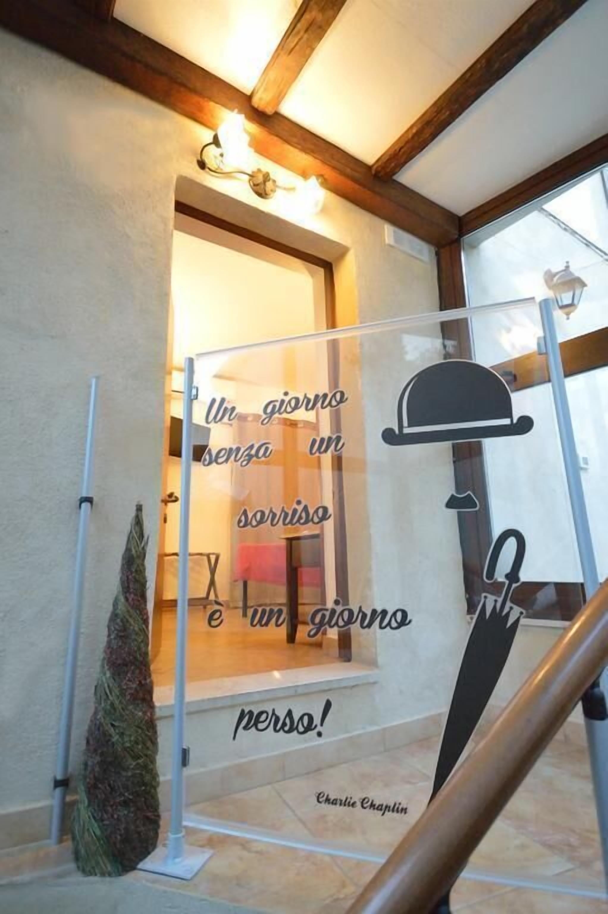 A glass door with a motivational quote in Italian, a small potted plant, and a staircase railing.