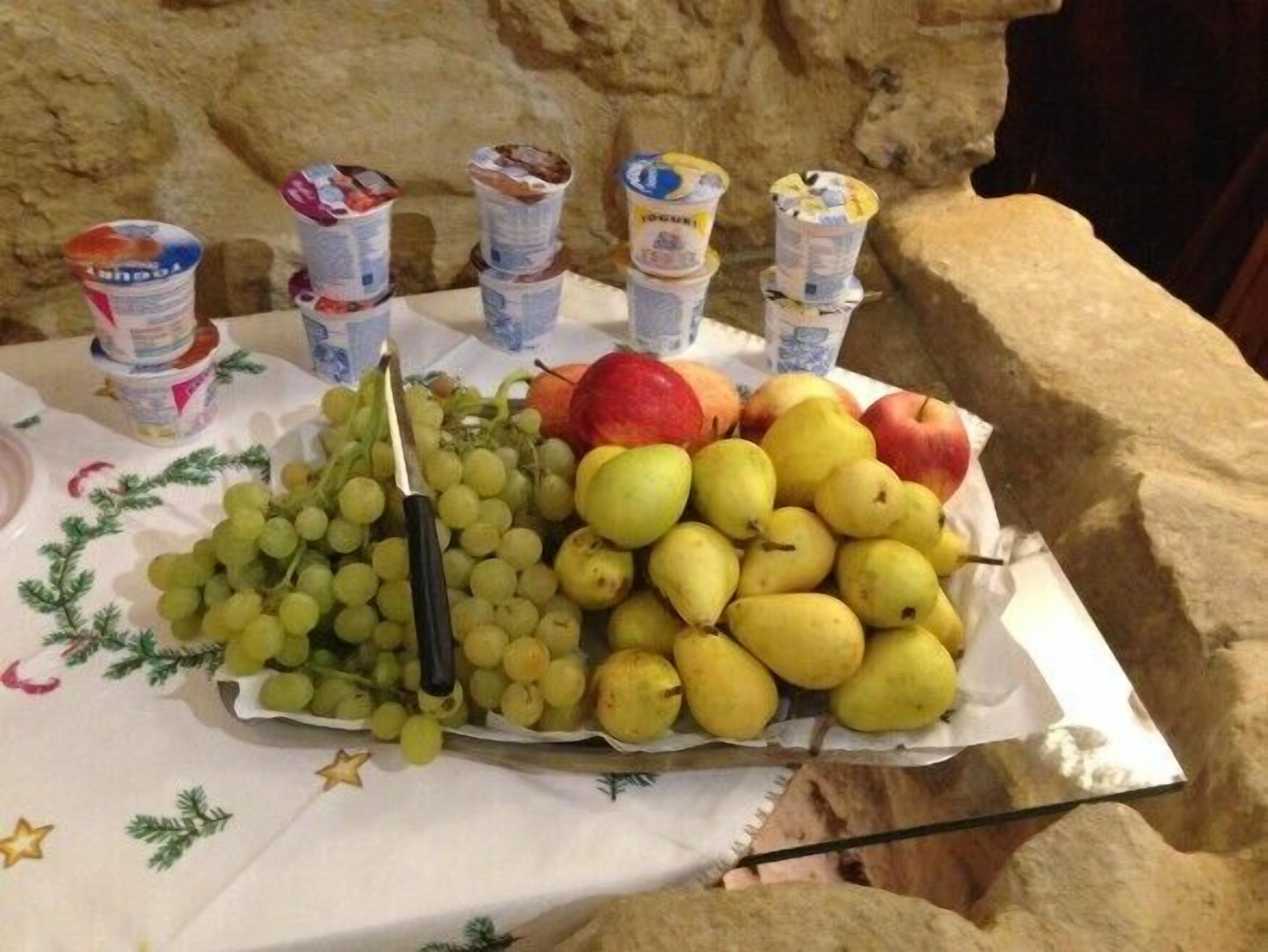 Un tavolo con un buffet di frutta e yogurt, con uva, pere, mele e vasetti di yogurt.