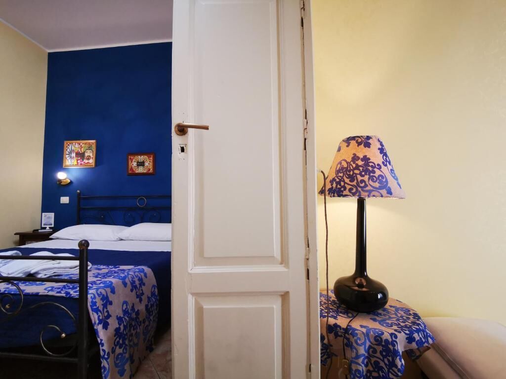 A room with a bed, a bedside table with a lamp, and a door.