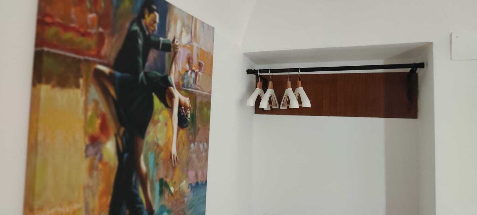 A room with a large abstract painting on the left wall and a black curtain rod with white and copper pendant lights on the right.