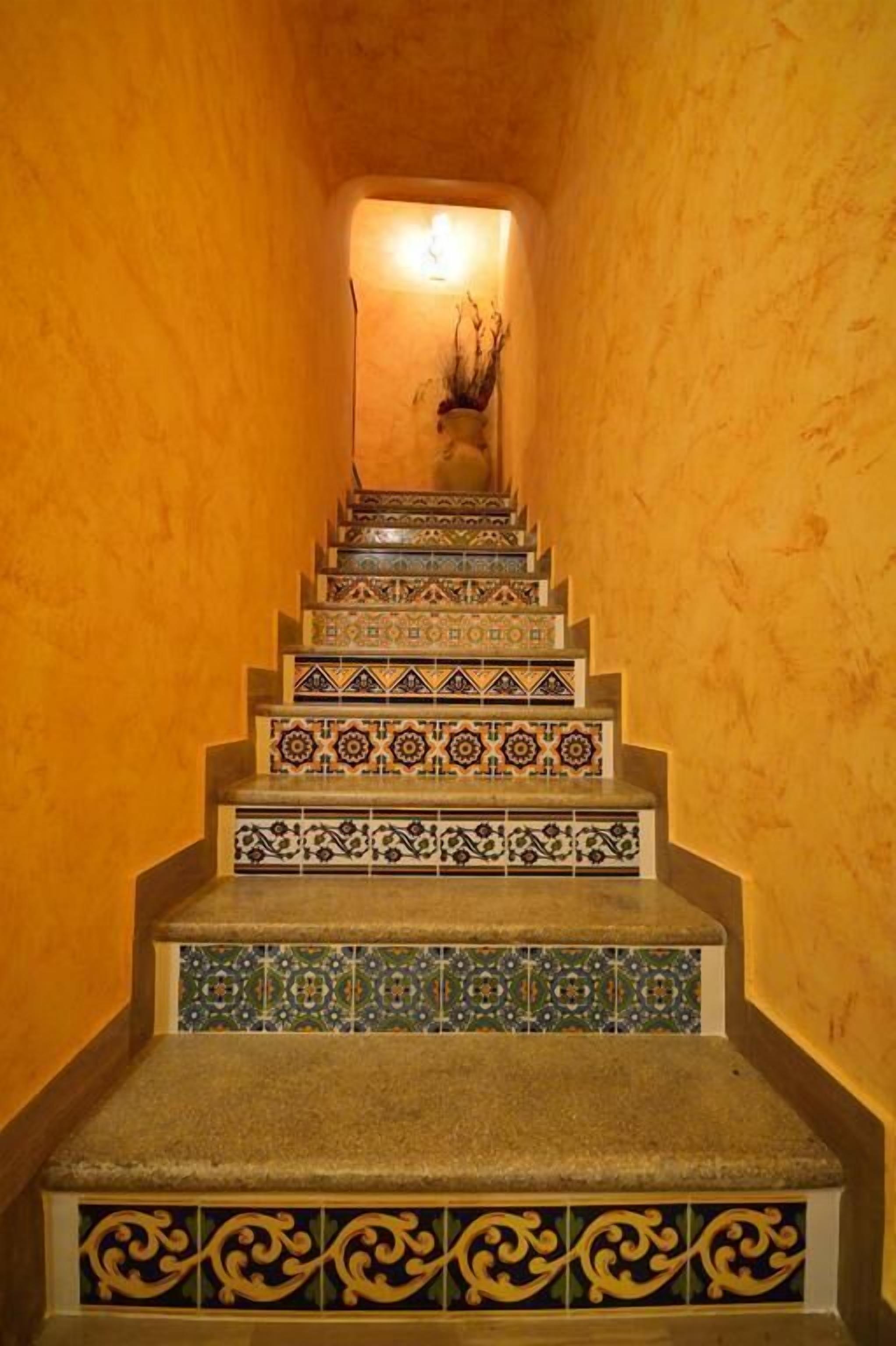 Una escalera con baldosas decorativas y con diseños, que lleva a una zona iluminada en la parte superior.