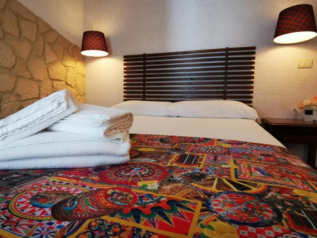 A neatly made bed with a colorful patterned bedspread, a folded white towel, and a wooden headboard.