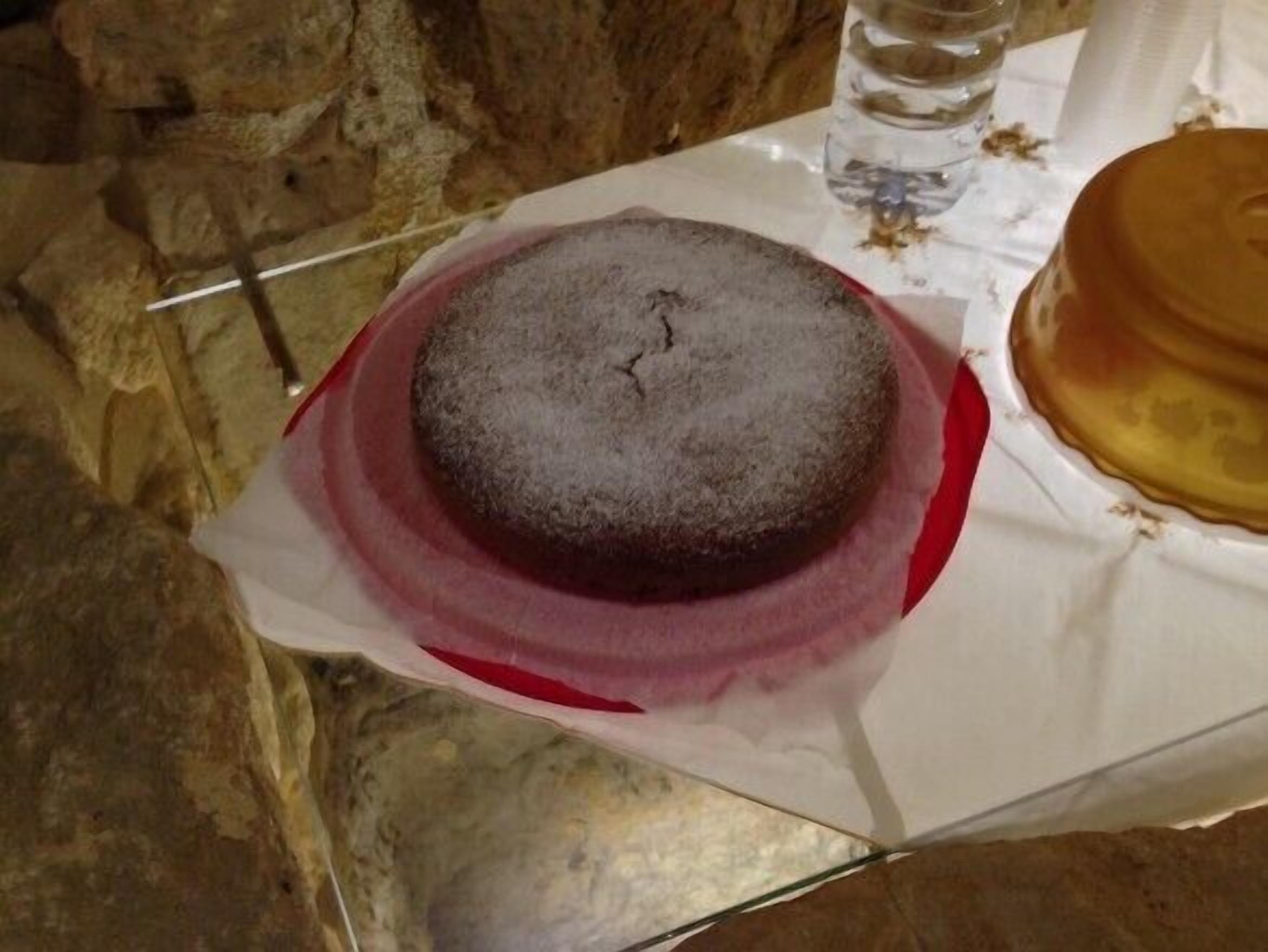 A round cake on a white tablecloth with a red rim, placed on a glass table.