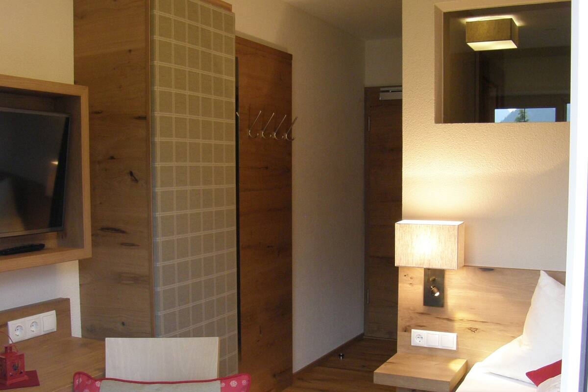A hotel room with a wooden floor, a television, a desk with a lamp, a chair with a cushion, and a bed with a floral bedspread.