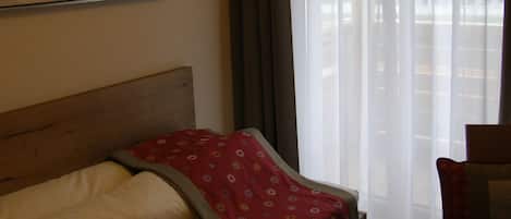 A hotel room with a bed, a chair, a painting on the wall, and a window with curtains.