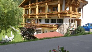 A wooden chalet with balconies, a stone facade, and a mountain backdrop.