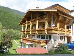 Un chalet de madera de varios pisos con balcones decorados con macetas de flores, al pie de montañas.