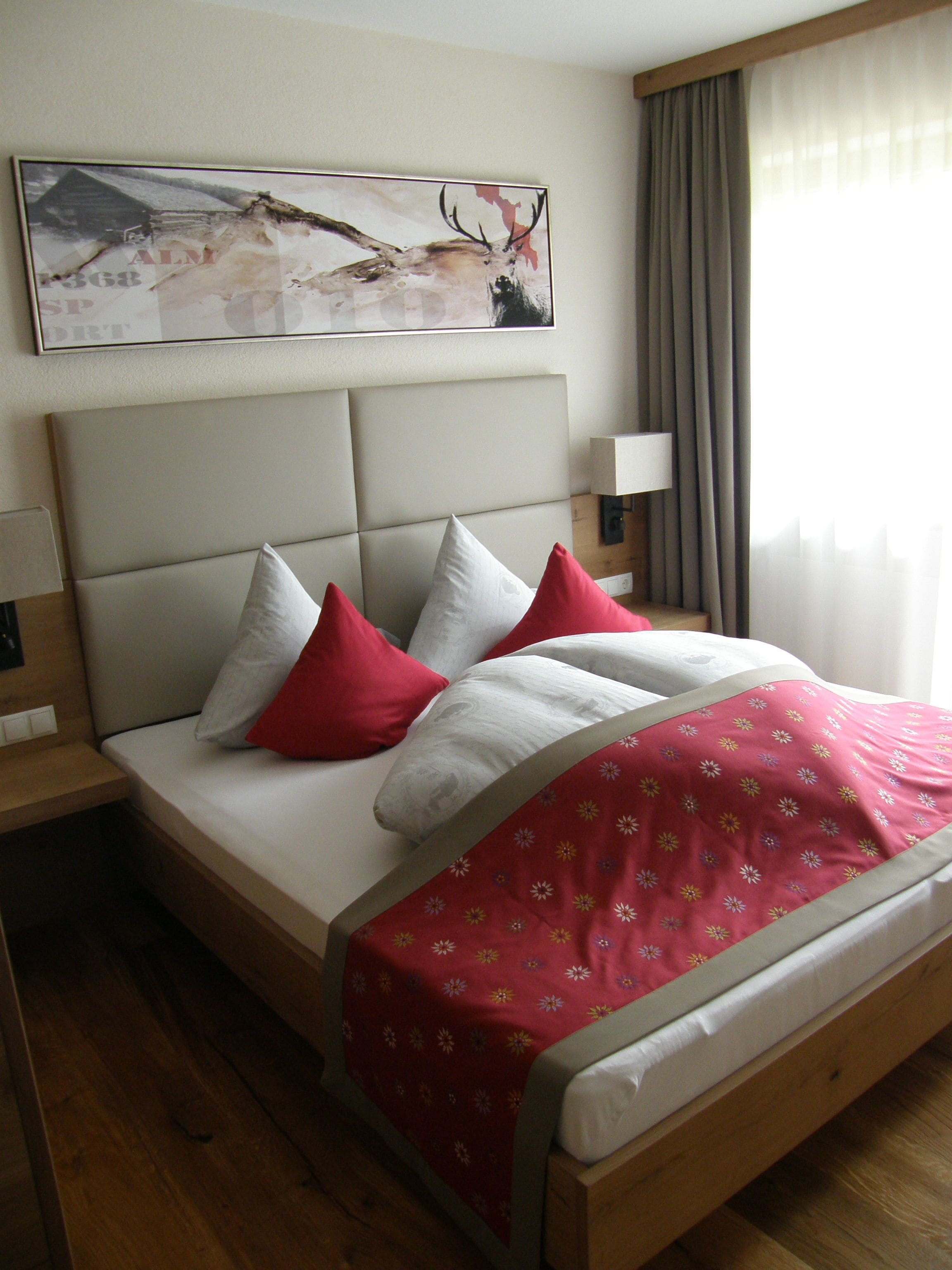 Une chambre d’hôtel avec un lit, des oreillers, une table de chevet, une lampe, un tableau au mur et une fenêtre avec des rideaux.