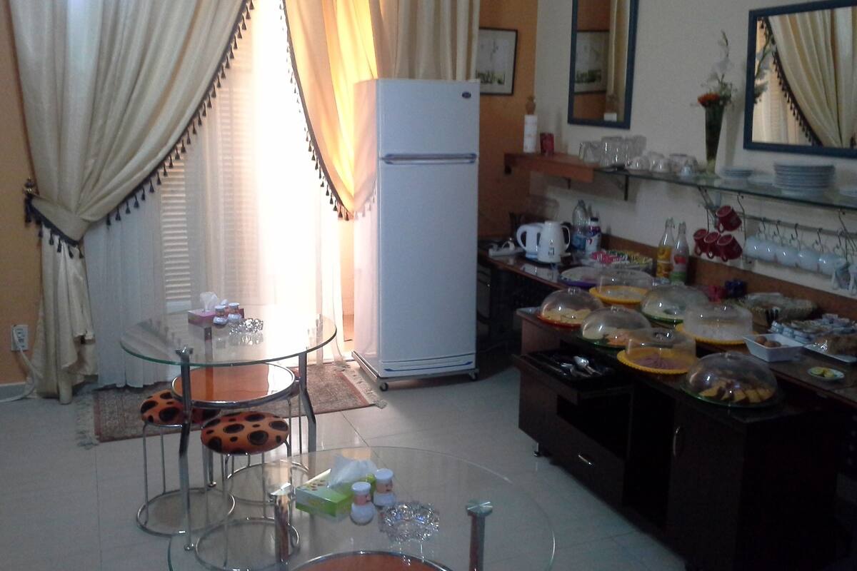 A kitchen with a refrigerator, a dining table with chairs, and a buffet setup.