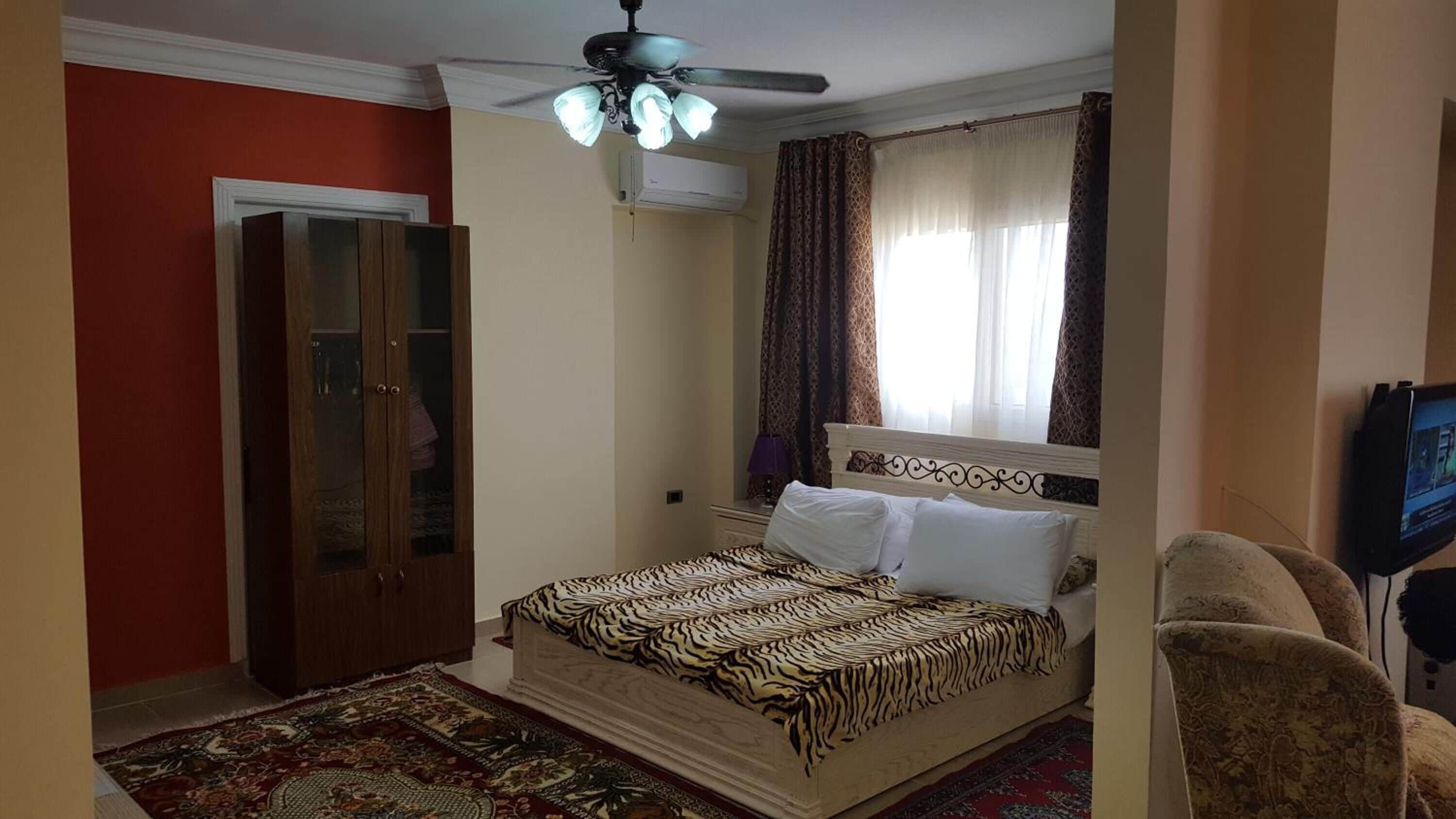 A bedroom with a bed, a wardrobe, a ceiling fan, and a television.