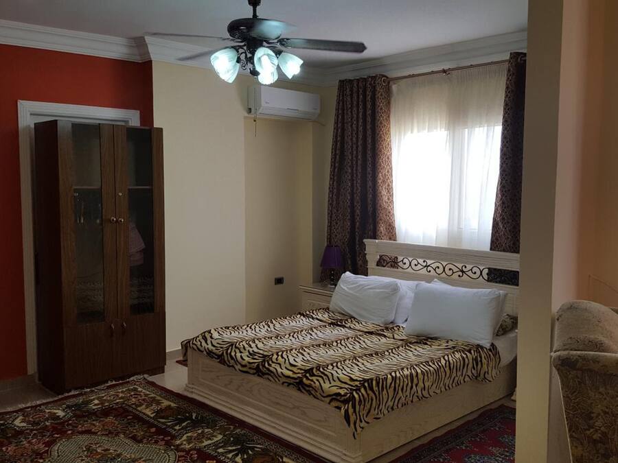 A bedroom with a bed, a wardrobe, a ceiling fan, and a television.