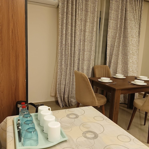 A dining area with a table set for two, a tray with water bottles and glasses, and curtains with a geometric pattern.