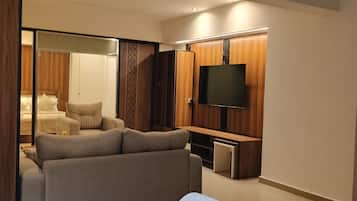 A modern living room with a sofa, a TV mounted on the wall, and a sliding door leading to a bedroom.