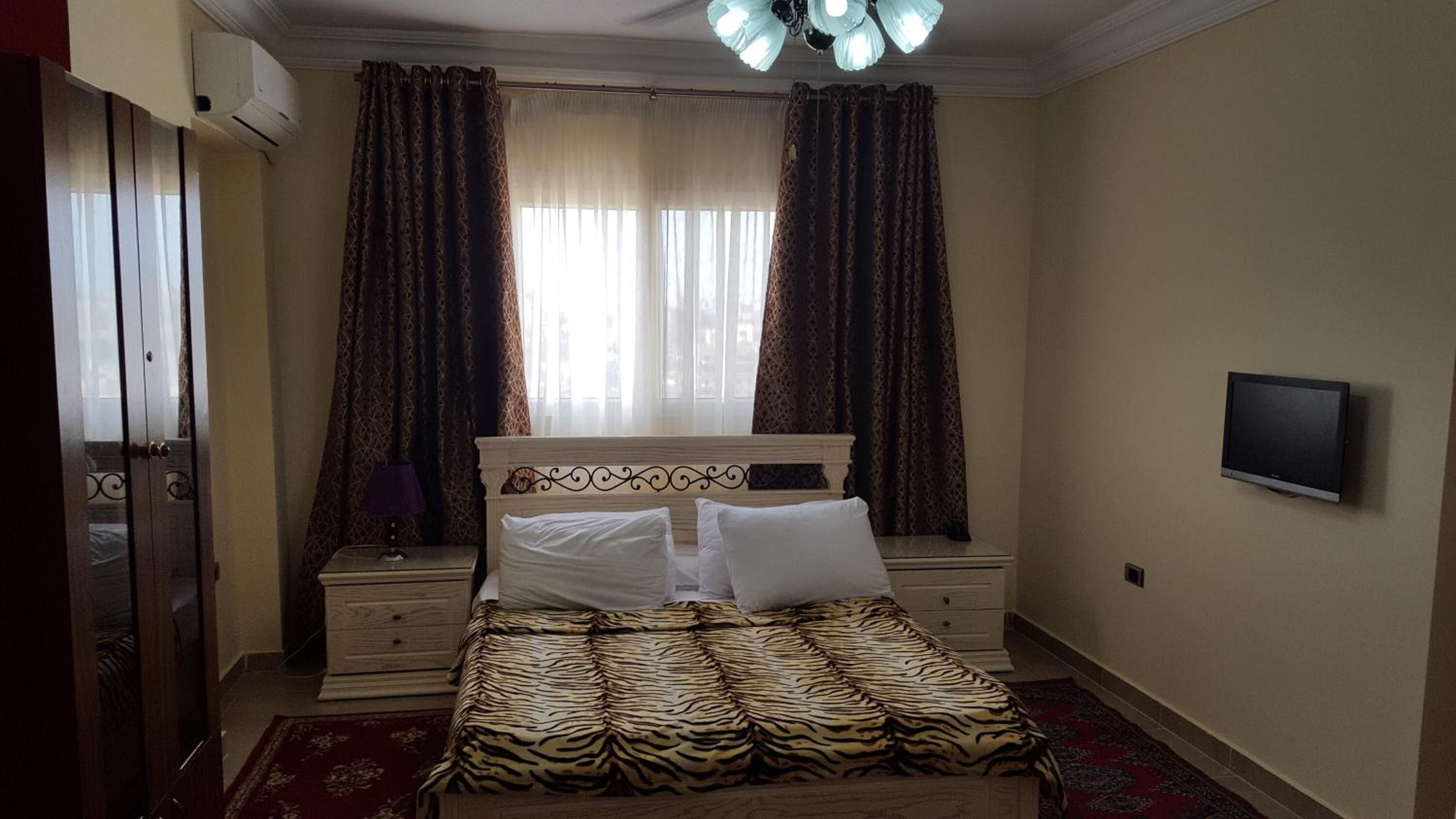 A bedroom with a bed, two nightstands, a television, and a window with curtains.