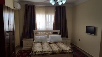 A bedroom with a bed, two nightstands, a television, and a window with curtains.
