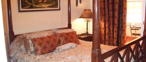 A bedroom with a four-poster bed, a painting on the wall, a lamp, and a window with curtains.