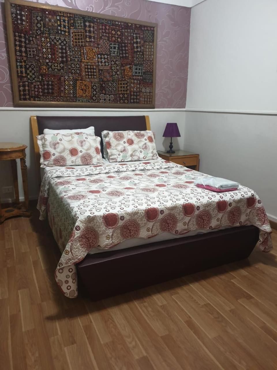 A bedroom with a bed, a nightstand, a lamp, and a wall tapestry.
