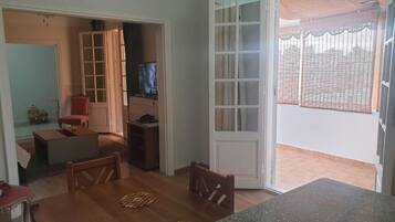 A dining area with a wooden table and chairs, a television in the background, and a sliding glass door leading to an outdoor balcony.