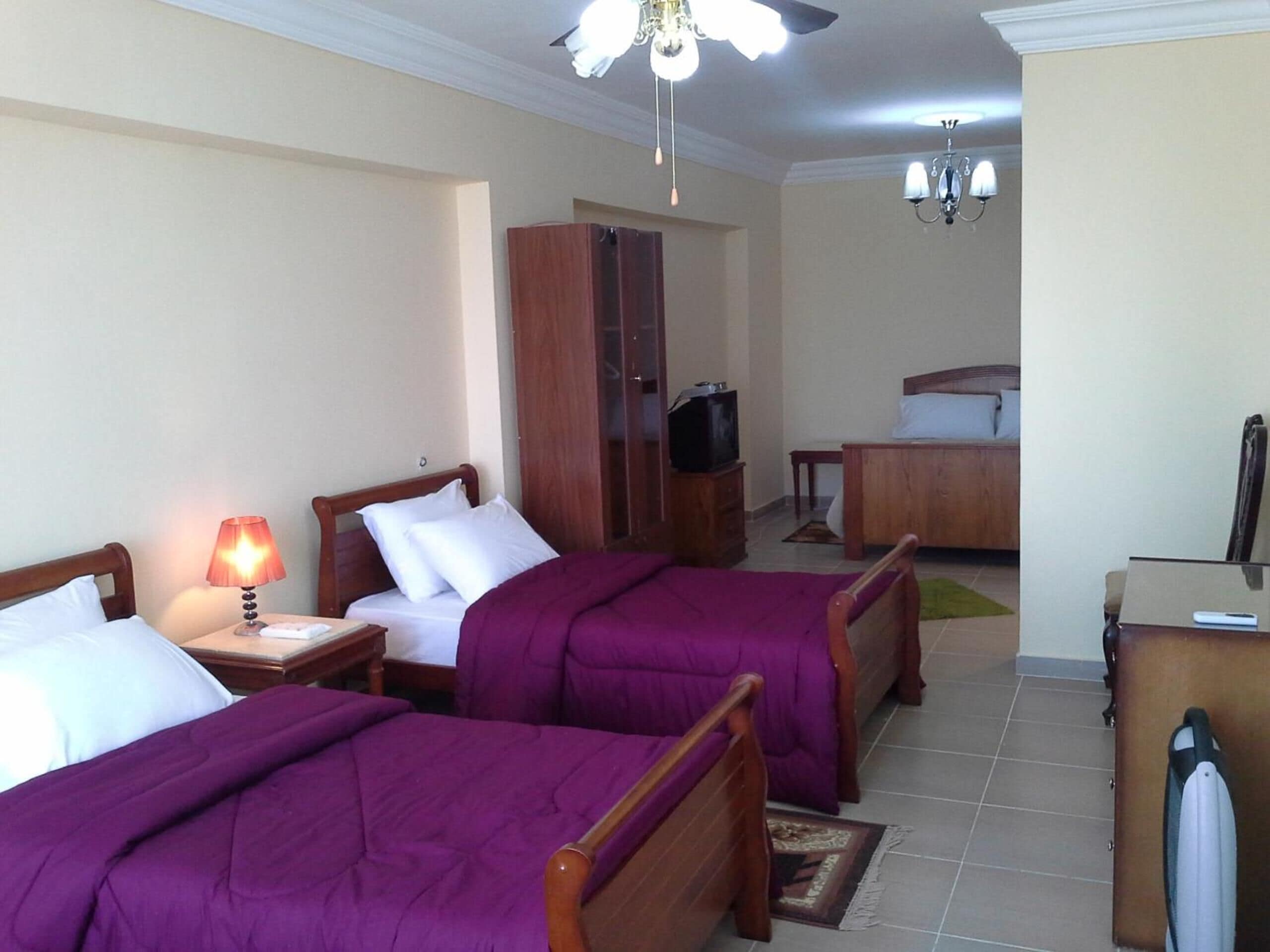 A hotel room with two beds, a desk, a wardrobe, a television, and a chandelier.