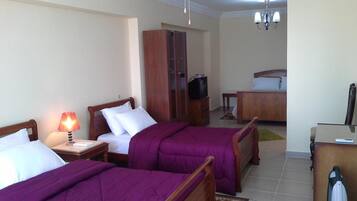 Quarto de hotel com duas camas, uma escrivaninha, um guarda-roupa, uma televisão e um candelabro.