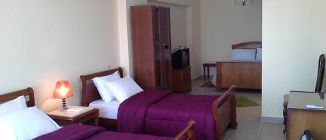 A hotel room with two beds, a desk, a wardrobe, a television, and a chandelier.