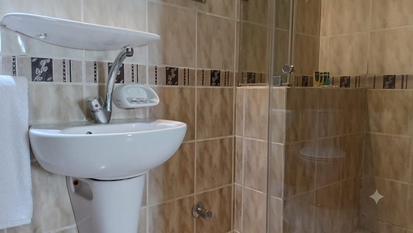 Un baño con lavamanos blanco, espejo y zona de ducha.