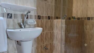 Un baño con lavamanos blanco, espejo y zona de ducha.
