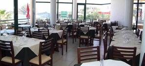 A restaurant with multiple tables set for dining, large windows, and a view of the outdoors. - Hotel Salgueiro (Porto Moniz)
