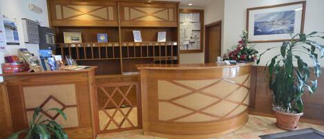 A reception area with a wooden reception desk, a potted plant, and a framed picture on the wall.