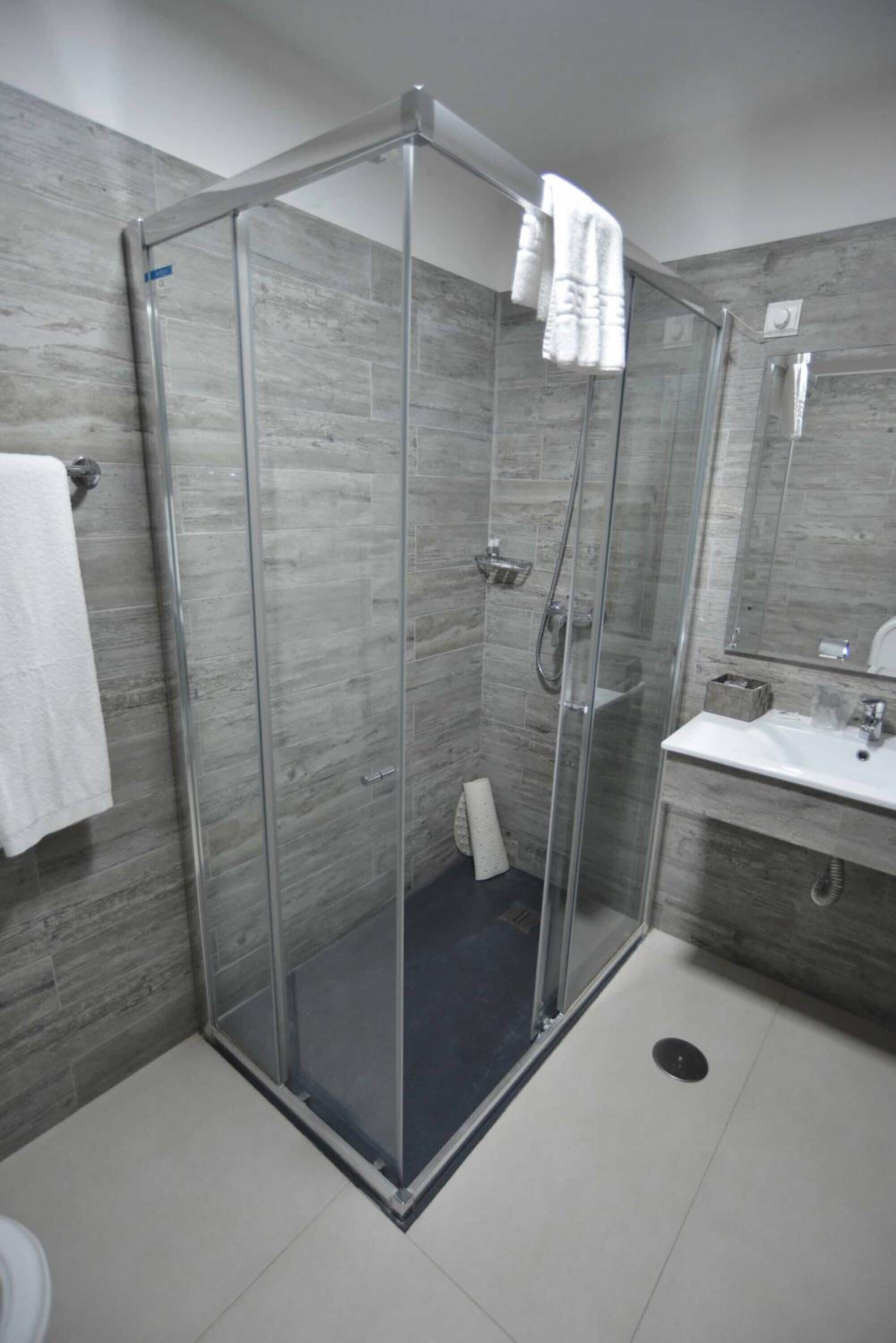 A modern bathroom with a glass-enclosed shower, a white sink, and a mirror.