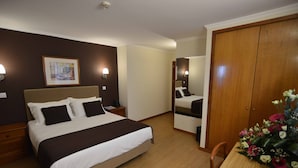 A hotel room with a large bed, bedside tables, a wooden wardrobe, and a mirror. - Hotel Salgueiro (Porto Moniz)