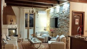 Uma sala de estar acolhedora com lareira, assentos confortáveis, uma parede de destaque em pedra e uma TV de tela plana.