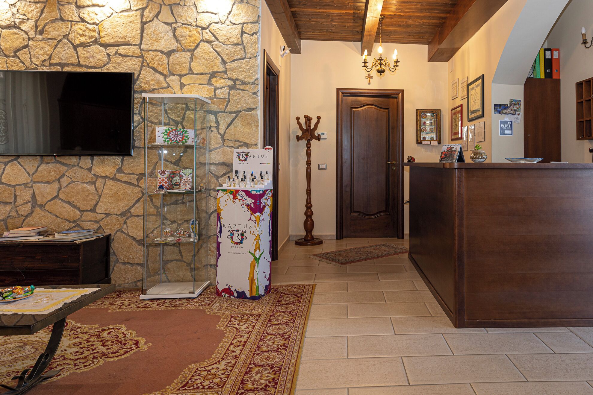 A well-lit hallway with a stone wall, a wooden door, a coat rack, and a reception desk with a sign.