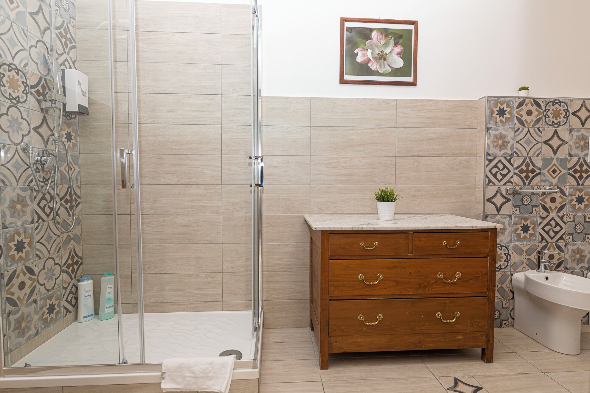 A bathroom with a shower, a wooden vanity with drawers, a toilet, and a framed picture on the wall.