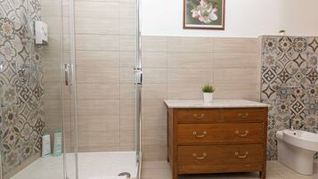 A bathroom with a shower, a wooden vanity with drawers, a toilet, and a framed picture on the wall.