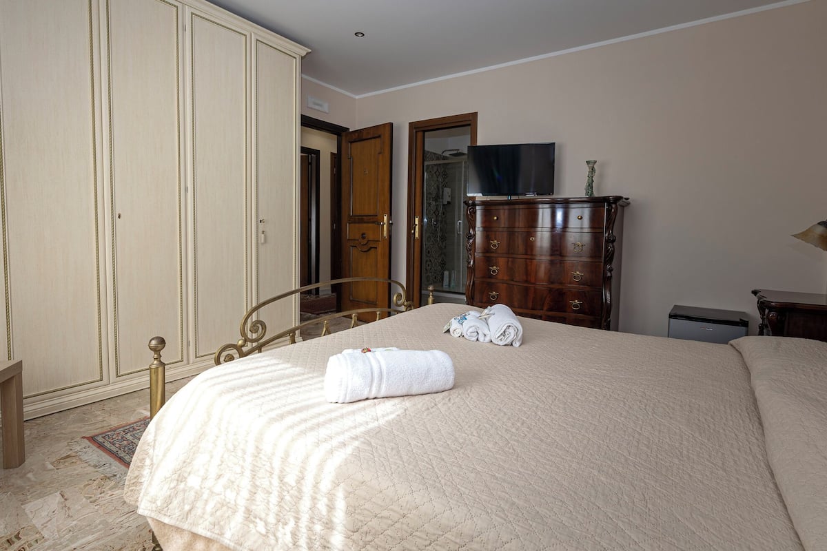 A neatly made bed with a quilt, a wooden dresser, and a wardrobe in a hotel room.
