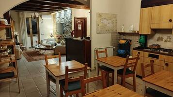 Un coin repas chaleureux avec des tables et des chaises en bois, une cuisine équipée d’une cuisinière et de placards, et un salon avec un canapé et une cheminée.