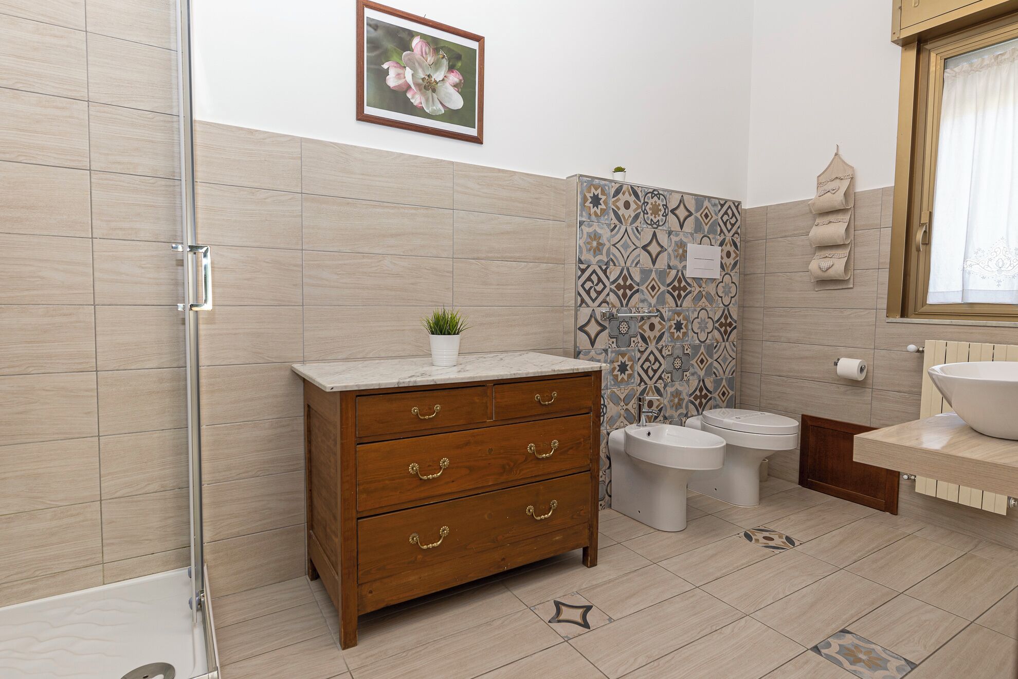 Une salle de bain avec un meuble-lavabo en bois, deux toilettes, un lavabo et une douche.