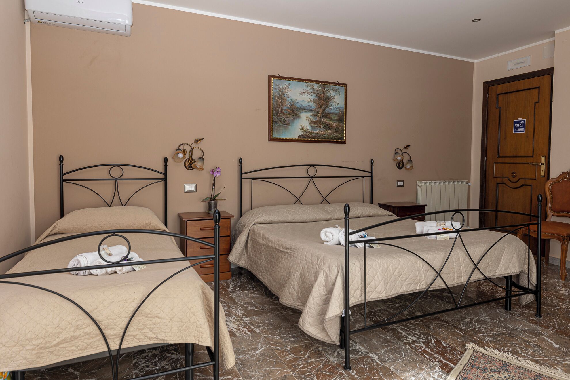 Una habitación de hotel con dos camas, un cuadro en la pared, una puerta de madera y un radiador.