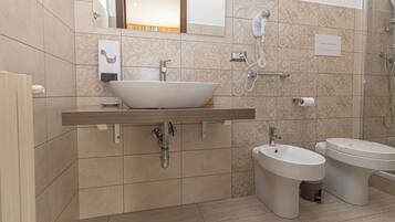 Ein modernes Badezimmer mit einem großzügigen Aufputzbecken, einem Bidet, einer Toilette und einem an der Wand befestigten Föhn.