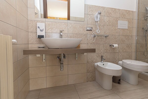 A modern bathroom with a large vessel sink, a bidet, a toilet, and a hairdryer mounted on the wall.