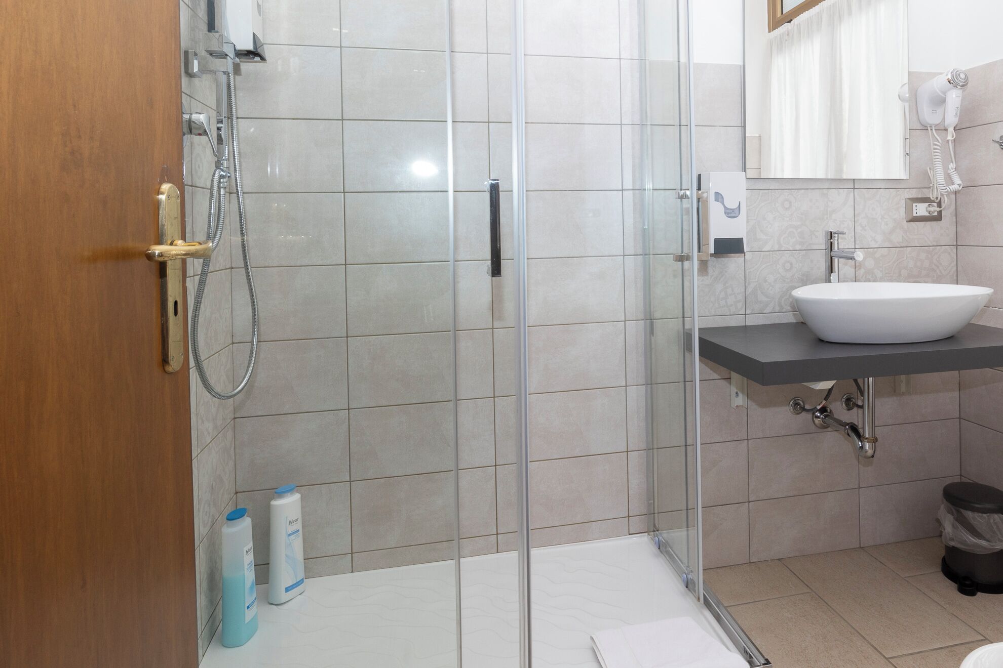 A modern bathroom with a glass shower enclosure, a white sink, and a mirror above it.