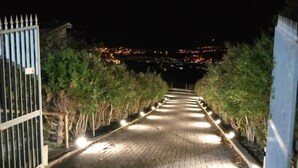 Uma trilha pavimentada conduz a um portão com vista para o horizonte urbano à noite.