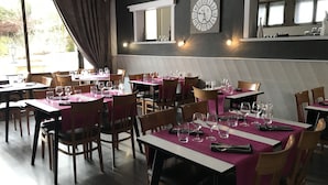 A restaurant with tables set for dining, a clock on the wall, and large windows.