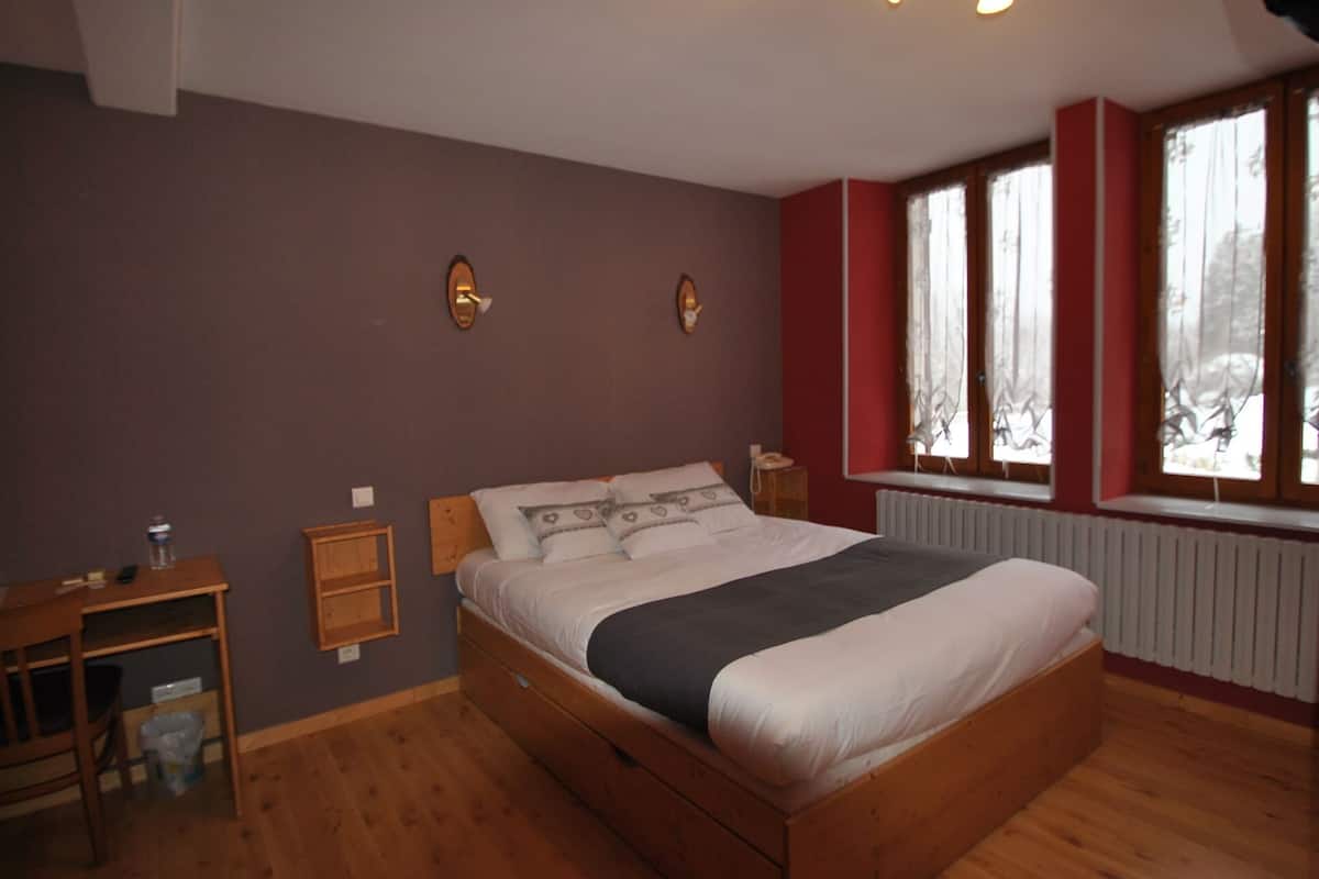 Une chambre à coucher avec un lit en bois, une table de chevet, un radiateur et une fenêtre avec des rideaux.