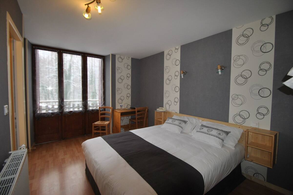 Une chambre à coucher avec un grand lit, un bureau, une chaise, un radiateur et une fenêtre avec des rideaux.