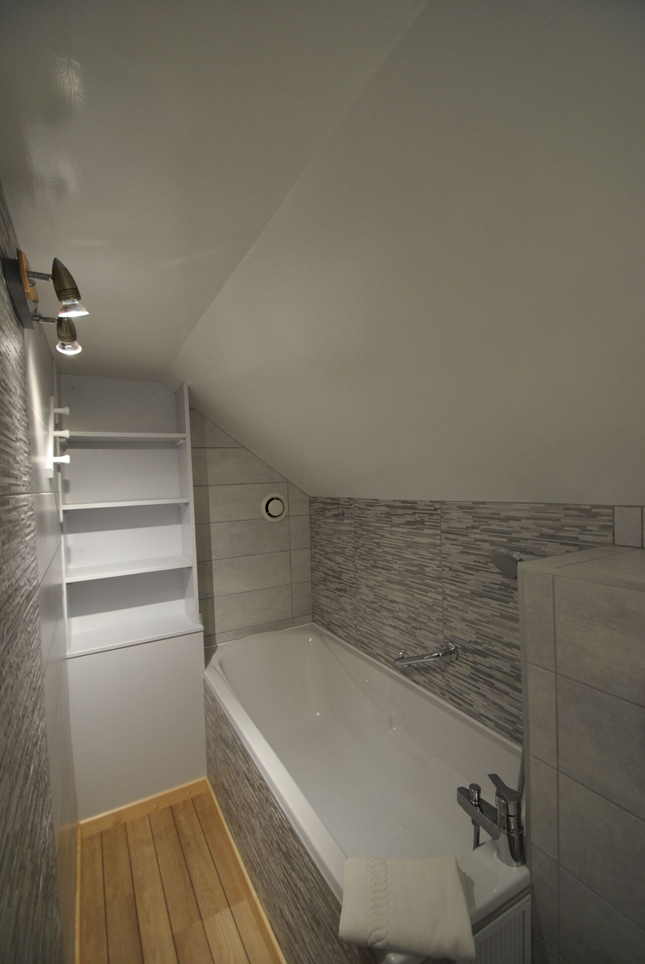 A modern bathroom with a built-in shower, a wooden floor, and a tiled wall.