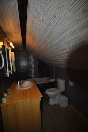 Un baño pequeño con tocador de madera, lavamanos blanco, inodoro y zona de ducha.
